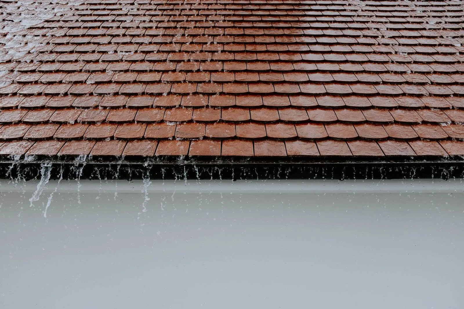 Heavy rain running off a roof edge and splashing down past the gutter during a downpour