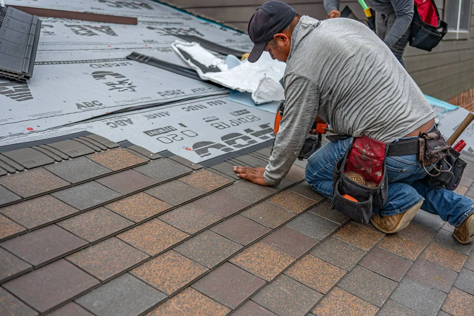 Roofer kneeling on a Clark County roof to repair shingles over fresh underlayment and flashing