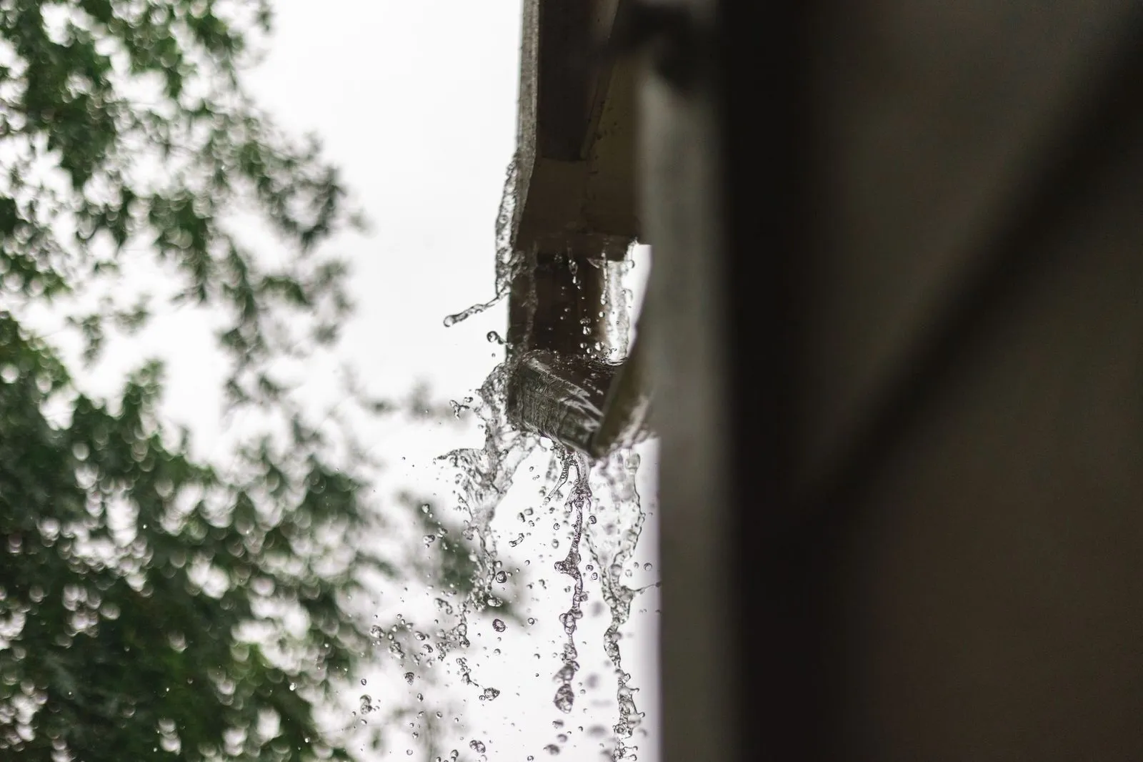 Rainwater pouring off the end of a gutter and downspout outlet during a fall downpour